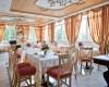 Prostorná restaurace s elegantním dřevěným stropem a červeno-žlutými závěsy.