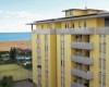 Žlutá budova s balkony poblíž pláže a tenisového kurtu.