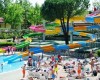 Aquapark se skluzavkami, bazénem a lidmi odpočívajícími na lehátkách.