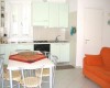 Malá kuchyně s bílou linkou, jídelní stůl se židlemi a oranžová pohovka.