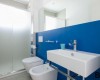 Moderní koupelna s modrou stěnou, umyvadlem, toaletou a bidetem.