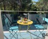 Dvě modré židle a žlutý stůl se snídaní na balkoně s výhledem do lesa.  