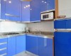 Moderní kuchyň s modrými lesklými skříňkami, vestavěnou mikrovlnnou troubou a ledničkou.