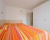 Ložnice s postelí s oranžovo-žlutým povlečením a bílou šatní skříní.