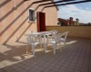 Plastový stůl se čtyřmi židlemi na střešní terase s dlažbou.