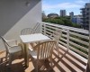 Balkón s plastovým stolem a čtyřmi židlemi, s výhledem na stromy a budovy.