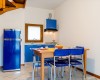 Kuchyň s modrými skříňkami a židlemi kolem dřevěného stolu.