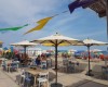 Kavárenská terasa s velkými deštníky u pláže s barevnými lehátky.