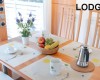 Dřevěný stůl se čtyřmi prostírkami, kávovarem, ovocem a květinami, s nápisem LODGE v rohu.