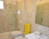 Koupelna s mozaikovými obklady, sprchovým koutem, umyvadlem, toaletou a žlutým ručníkem.