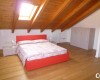 Ložnice v podkroví s dřevěnými trámy, červenou postelí, a bílým nábytkem.