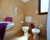 Koupelna s umyvadlem, toaletou a bidetem, vybavená fialovými ručníky.