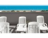 Bílé plastové lehátka na terase s výhledem na pláž a moře.