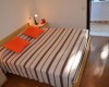 Ložnice s manželskou postelí, pruhovaným přehozem a dvěma oranžovými polštáři.