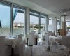 Moderní restaurace s bílými ubrusy a velkými okny s výhledem ven.