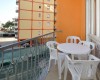 Balkón s plastovým stolem a židlemi, výhled na oranžovou budovu.