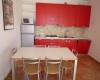 Kuchyně s červenými skříňkami, jídelním stolem a čtyřmi židlemi.