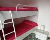 Poschoďová postel s červeným povlečením a nočním stolkem s lampičkou.