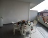 Zastřešený balkon s kulatým stolem pokrytým ubrusem a čtyřmi plastovými židlemi.