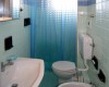 Koupelna se světle modrými kachličkami, umyvadlem, toaletou a bidetem, oddělená sprchovým závěsem.