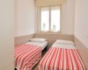 Dvě jednolůžkové postele s červeno-bílými pruhovanými přehozy v malé místnosti.