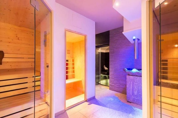 Moderní wellness s dřevěnou saunou a kamennou stěnou osvětlenou modrým světlem.