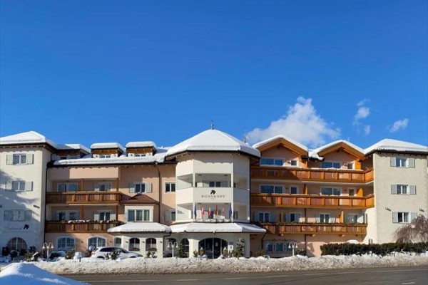 Velký hotel s balkony za zimního dne na zasněžené ulici a modré obloze.