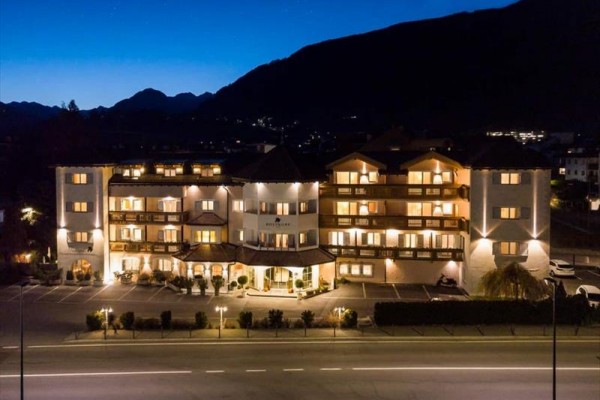 Osvětlený hotel večer s horami na pozadí.  