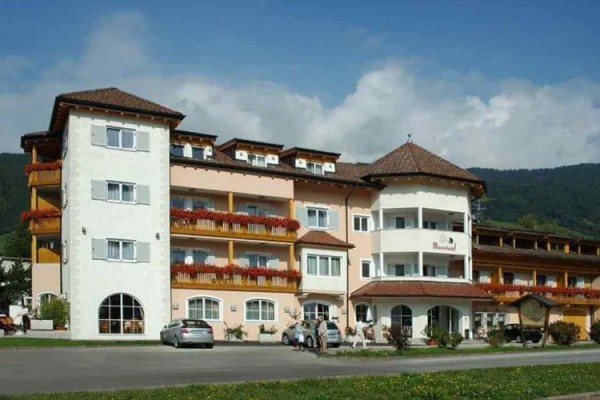 Velký třípatrový hotel se žlutými a bílými fasádami, balkony a zaparkovanými auty před budovou.