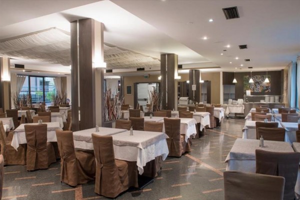 Prostorná restaurace s hnědými židlemi a bílými ubrusy na stolech.  
