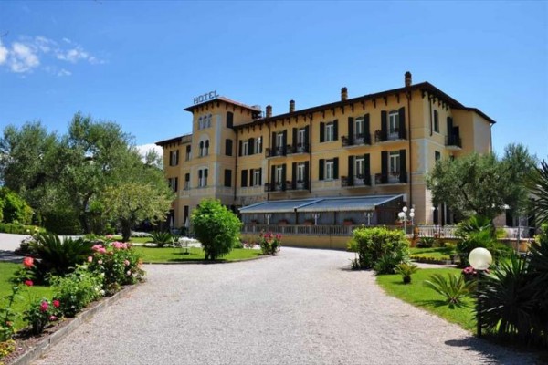 Velký hotel uprostřed upravované zahrady s květinami a stromy.