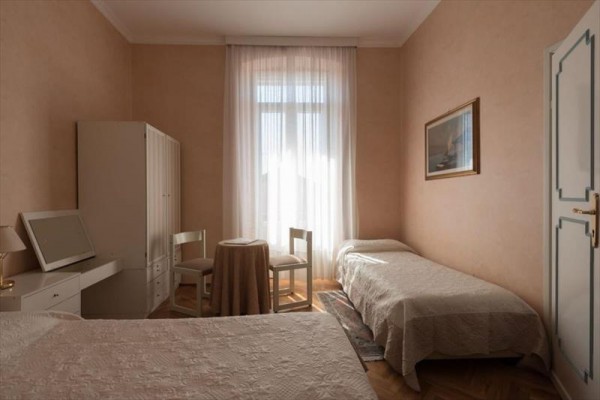 Ložnice se dvěma postelemi, stolem a dvěma židlemi, vedle okna s průsvitným závěsem.
