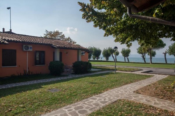 Jednopatrový dům s oranžovou fasádou obklopený zelení s výhledem na jezero.