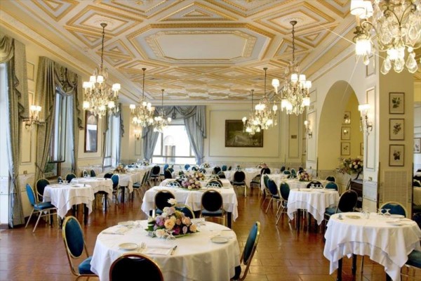 Elegantní jídelna s kulatými stoly, květinovými dekoracemi a lustry.