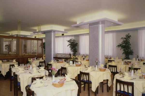 Prostorná restaurace s kulatými stoly zakrytými žlutými ubrusy.