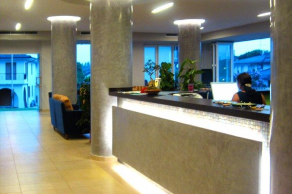Luxusní hotelová recepce s moderním osvětlením a halou, kde u stolu sedí osoba.