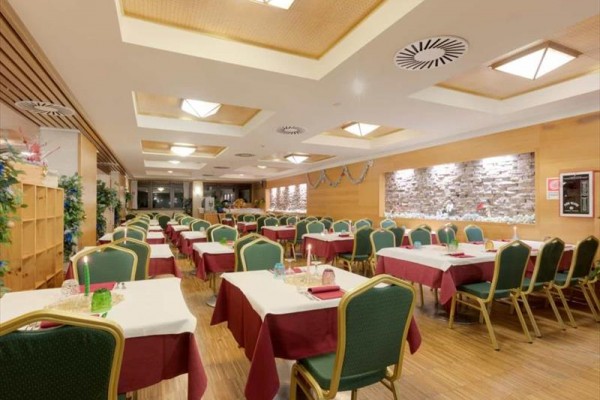 Restaurace s řadami stolů s bílými ubrusy a zelenými židlemi.