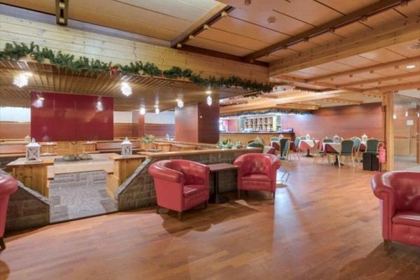 Interiér dřevěné restaurace s červenými křesly, vánoční dekorace a bar.