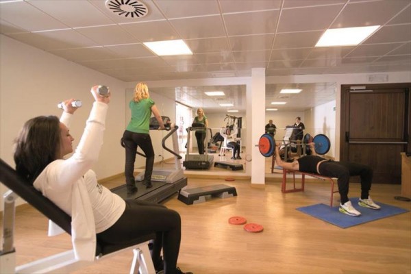 Lidé cvičí v posilovně s různým fitness vybavením.