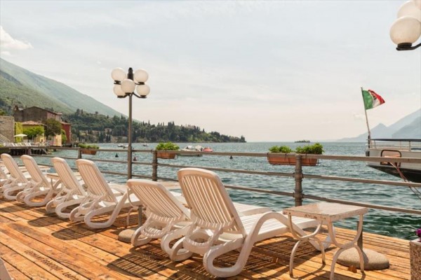 Lehátka na dřevěné terase s výhledem na jezero, v pozadí italská vlajka.