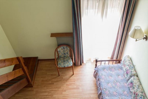 Místnost s dřevěnou podlahou, stolem, židlí a gaučem vedle velkého okna se záclonami.