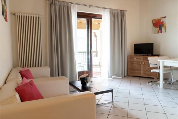 Světlý obývací pokoj s bílou pohovkou, stolem, televizí a francouzskými dveřmi na balkon.
