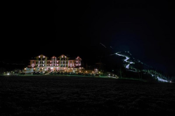Osvětlený hotel v noci s osvětlenou horskou cestou v pozadí.