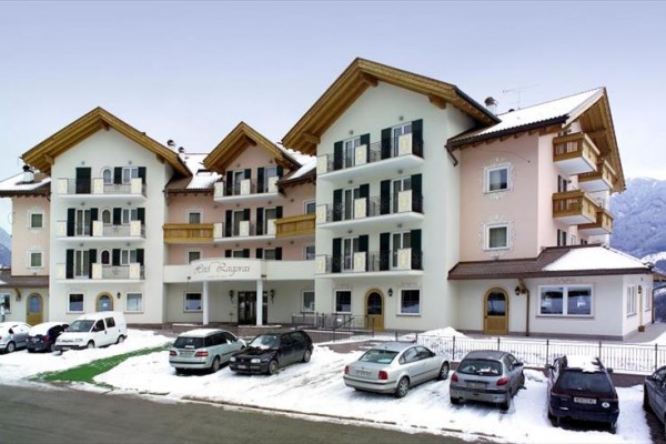 Budova hotelu s parkovištěm zasněženou zimní krajinou v pozadí.
