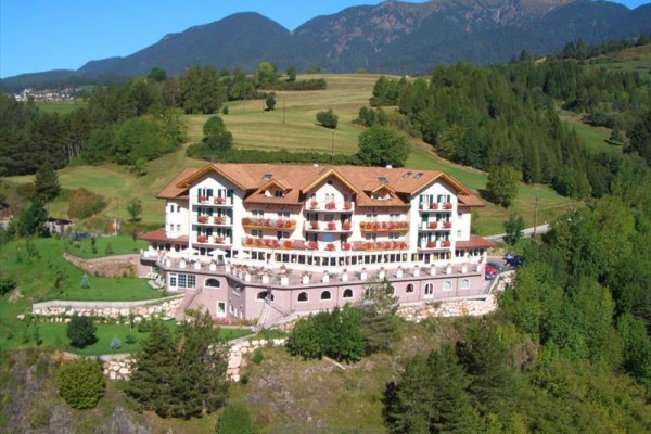 Velký horský hotel obklopený zelení s horami v pozadí.