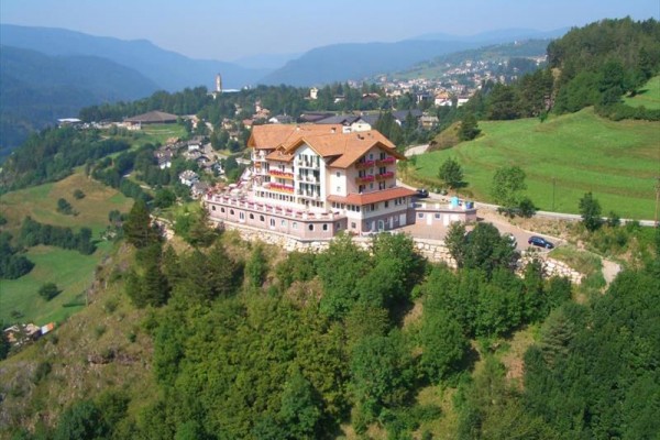 Hotel na vrcholu kopce obklopený zelenými loukami a lesy.