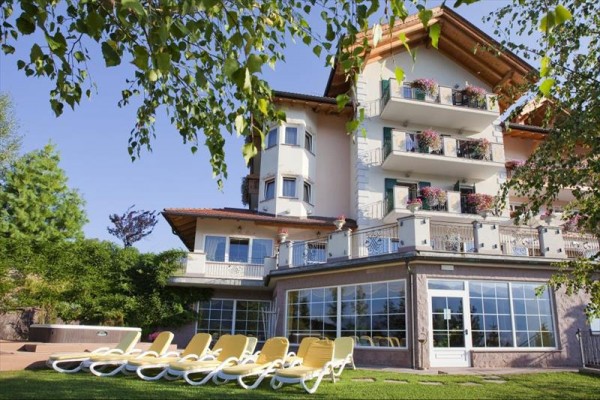 Budova hotelu s balkonem ozdobena květinami a lehátky v zahradě.