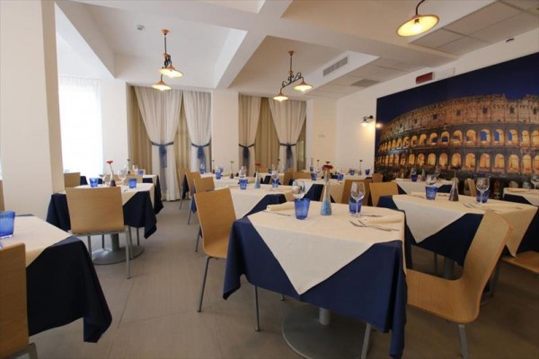 Elegantní restaurace s modro-bílými ubrusy a velkým obrazem Kolosea na zdi.