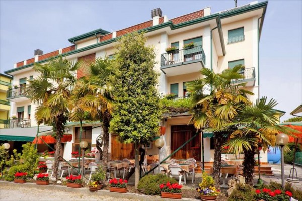 Budova s balkony obklopená palmami a kvetoucími květinami.