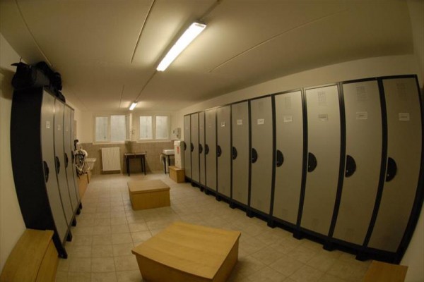 Šatna s řadami šedých skříněk a dřevěnými lavicemi uprostřed.